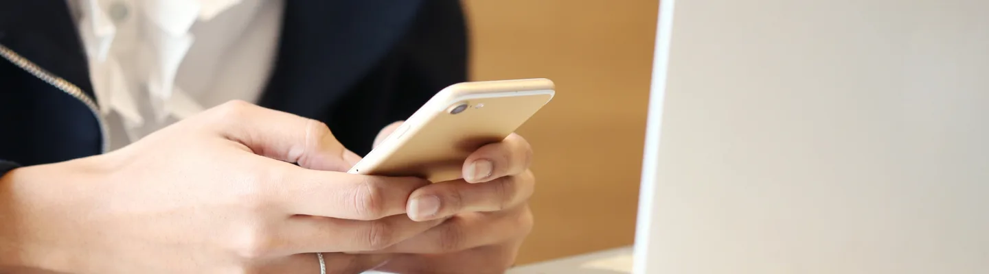 Close-up of a person holding a smartphone while sitting in front of a laptop